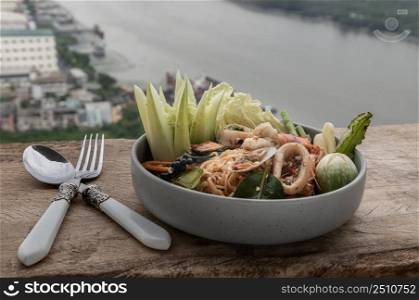 Spicy Stir Fried seafood Instant Noodles with herbs with various spices served with vegetables, cucumber, thai eggplant, chinese cabbage, white turmeric, winged bean and yardlong bean in ceramic plate. Selective focus.