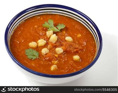 Spicy tomato and chickpea soup in a traditional Tunisian bowl with a spoon, garnished with parsley.