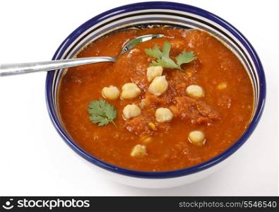Spicy tomato and chickpea soup in a traditional Tunisian bowl with a spoon, garnished with parsley.