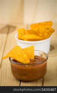 spicy tortilla chips and tomato salsa dip over wooden board