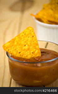 spicy tortilla chips and tomato salsa dip over wooden board