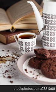 Spilled coffee on the table. Still life composition of chocolate cookies on the plate, coffee cup, coffee pot and books. Food photography. Coffee break