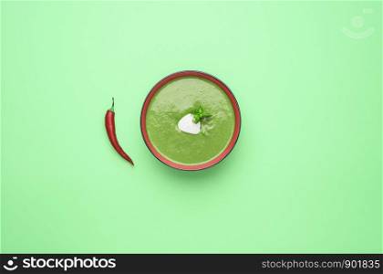 Spinach cream soup bowl with red chili pepper on a green background. Flat lay of tasty homemade vegetable soup. Minimal soup bowl from spinach.
