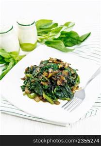 Spinach fried with onions in a plate on a napkin on background of white wooden board