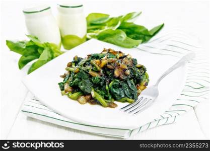 Spinach fried with onions in a plate on a towel against light wooden board