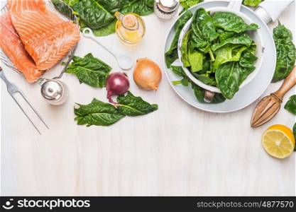 Spinach leaves and salmon fillets with ingredients on white kitchen table background, cooking preparation, top view, border. Diet nutrition and healthy food concept
