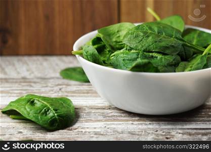 Spinach leaves close up in a bowl on a rustic wooden table.