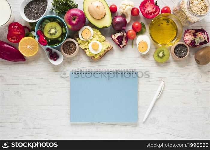 spiral book pen fresh fruits toasted bread vegetables ingredients white textured background