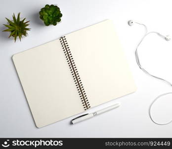 spiral notebook with empty sheets, pen and green plants in a pot, white table, workplace, copy space