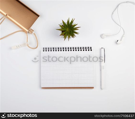 spiral notebook with white empty sheets, pen and green plants in a pot, white table, workplace, copy space
