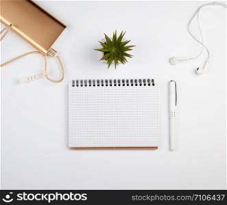 spiral notebook with white empty sheets, pen and green plants in a pot, white table, workplace, copy space