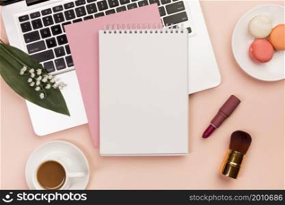 spiral notepad laptop with macaroons coffee cup with makeup brushes colored backdrop