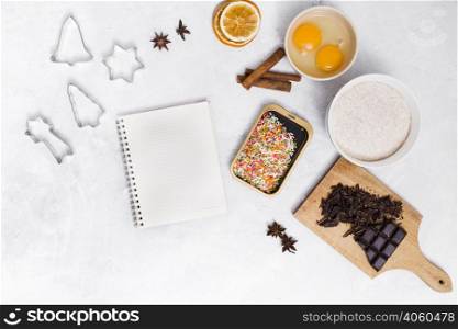 spiral notepad with colorful sprinkles pastry cutter star anise cinnamon dried citrus egg yolk chocolate bar white backdrop