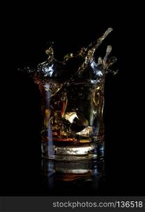 Splash from an ice cube in glass of whiskey isolated on black background. Splash from ice cube in glass of whiskey