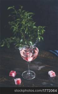 Splash of pink rose champagne in Elegant glass with frozen raspberries in ice cube on dark wooden table surface, close up, shallow depth of the field