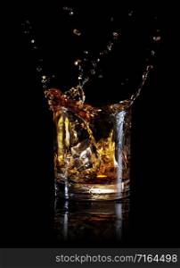 Splash of whiskey from an ice cube in a glass. Isolated on black background. Splash of whiskey from an ice cube in glass