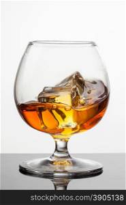 Splash of whiskey with ice in glass isolated on white background. Raw image, no postproduction