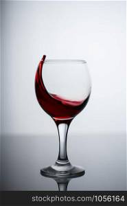 splashes of red wine in a glass on a black glossy glass on a white background