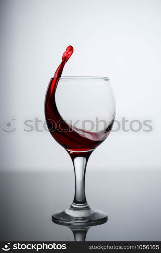 splashes of red wine in a glass on a black glossy glass on a white background