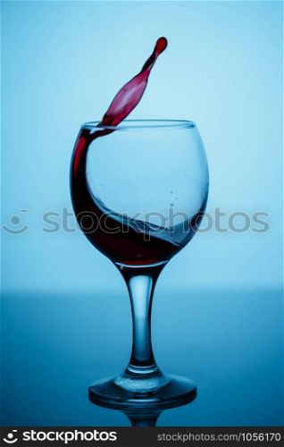 splashes of red wine in a glass on a black glossy glass on a blue background