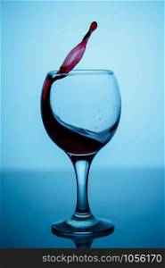 splashes of red wine in a glass on a black glossy glass on a blue background