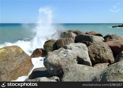 Splashing sea water on the rocks on the beach in Kamari in Greece.