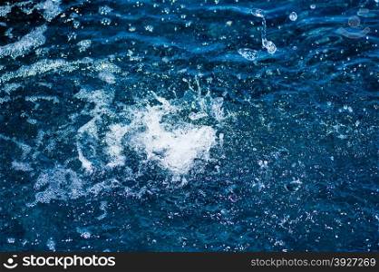 Splashing water and droplets impacting dark blue water surface in white splashes and foam.