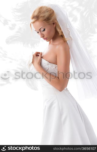 splendid bride with blonde hair in sensual pose wearing elegant dress, veil and floral decoration on hand. Feathered pattern on background