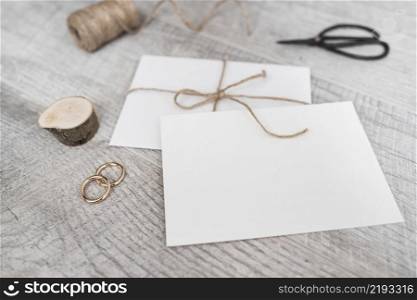 spool miniature tree stump wedding rings scissor white envelope wooden background