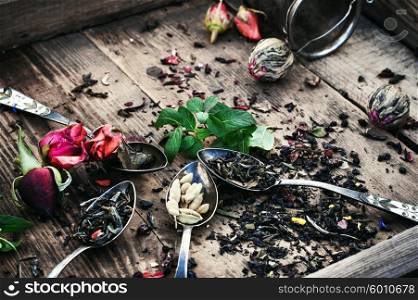 Spoon and spilling the tea leaves of different varieties on retro background. Scattered tea leaves