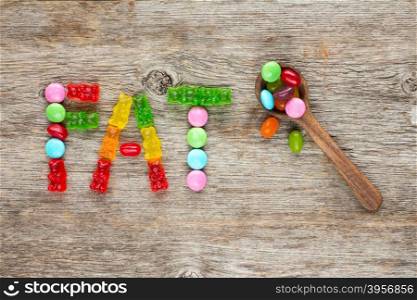 "Spoon and word made of candies "FAT" on the wooden background"