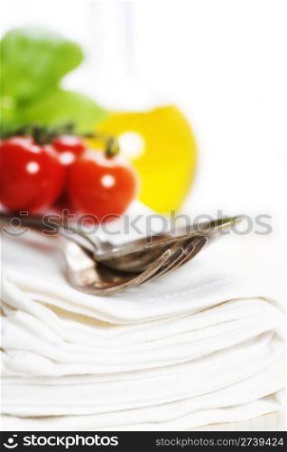 Spoon, fork, napkin and pasta ingredients (olive oil, basil, tomato)