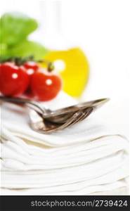 Spoon, fork, napkin and pasta ingredients (olive oil, basil, tomato)