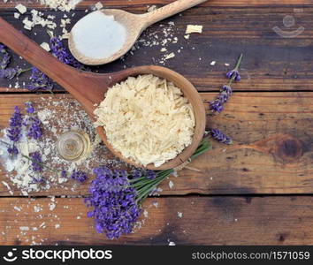 spoon full of flakes of soap with essential oil and bunch of lavender flowers on wooden background