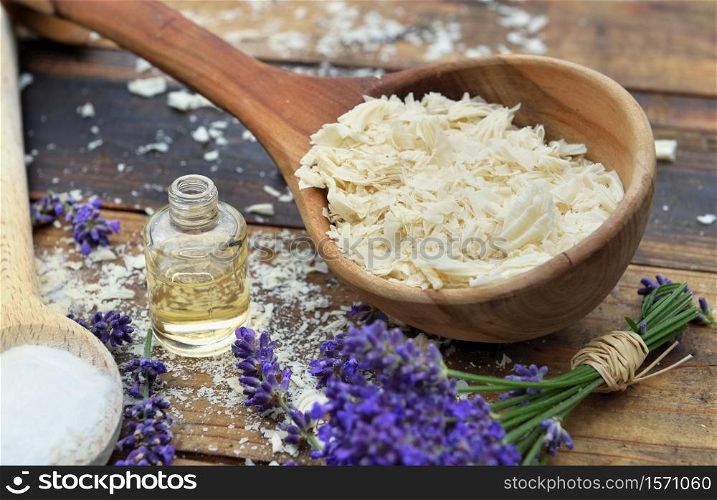 spoon full of flakes of soap with essential oil and bunch of lavender flowers on wooden background