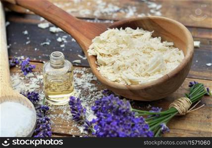 spoon full of flakes of soap with essential oil and bunch of lavender flowers on wooden background