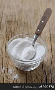 Spoon of baking soda in glass of baking soda on wooden table. Bicarbonate of soda.