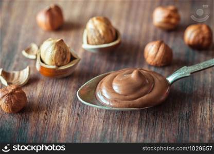Spoon of chocolate paste with hazelnuts on the wooden background