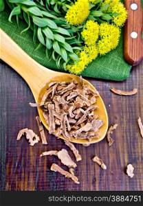 Spoon with dry roots of Rhodiola rosea, knife, fresh flowers Rhodiola rosea on a dark wooden board