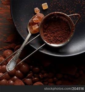 spoon with Turkish Delight and Cocoa powder in a sieve on a black plate, dark background. Turkish Delight and cocoa powder