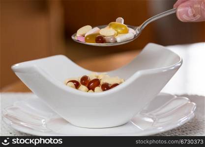 Spoonful of vitamin tablets suspended over bowl of tablets for breakfast in kitchen