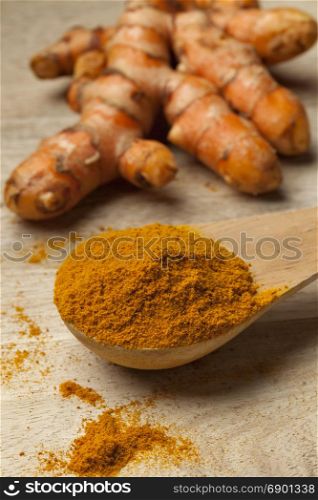 Spoonful turmeric powder with a fresh root at the background