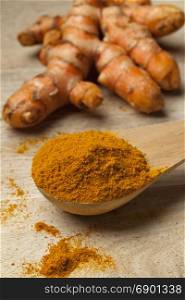 Spoonful turmeric powder with a fresh root at the background
