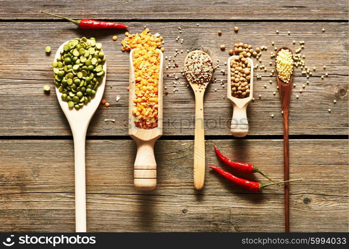 Spoons of various legumes on wooden background