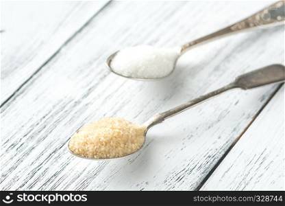 Spoons of white and brown sugar on the wooden background