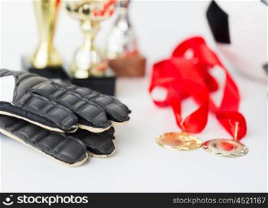sport, achievement, championship and success concept - close up of football or soccer ball and goalkeeper gloves with golden medals and cups