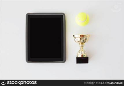 sport, achievement, championship and technology concept - close up of tennis ball, golden cup and tablet pc computer with black blank screen over white background from top