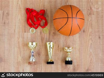 sport, achievement, championship, competition and success concept - basketball ball with golden medals and cups over wooden background