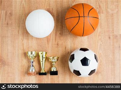 sport, achievement, championship, competition and success concept - close up of different balls and golden cups over wooden background