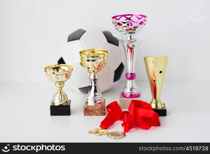 sport, achievement, championship, competition and success concept - close up of football or soccer ball with golden medals and cups over white background